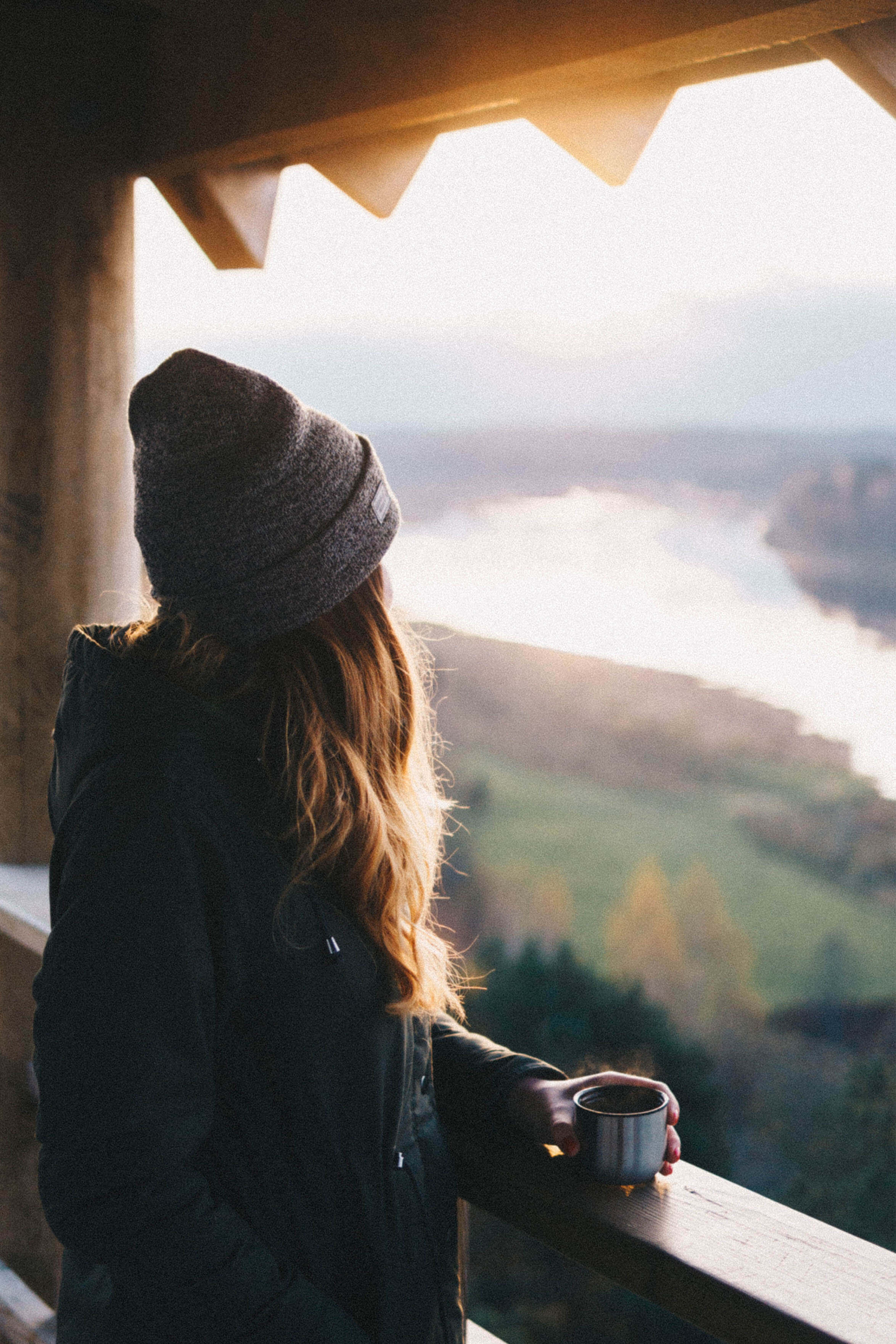 young woman with a mug of coffee gazing into distance over landscape.