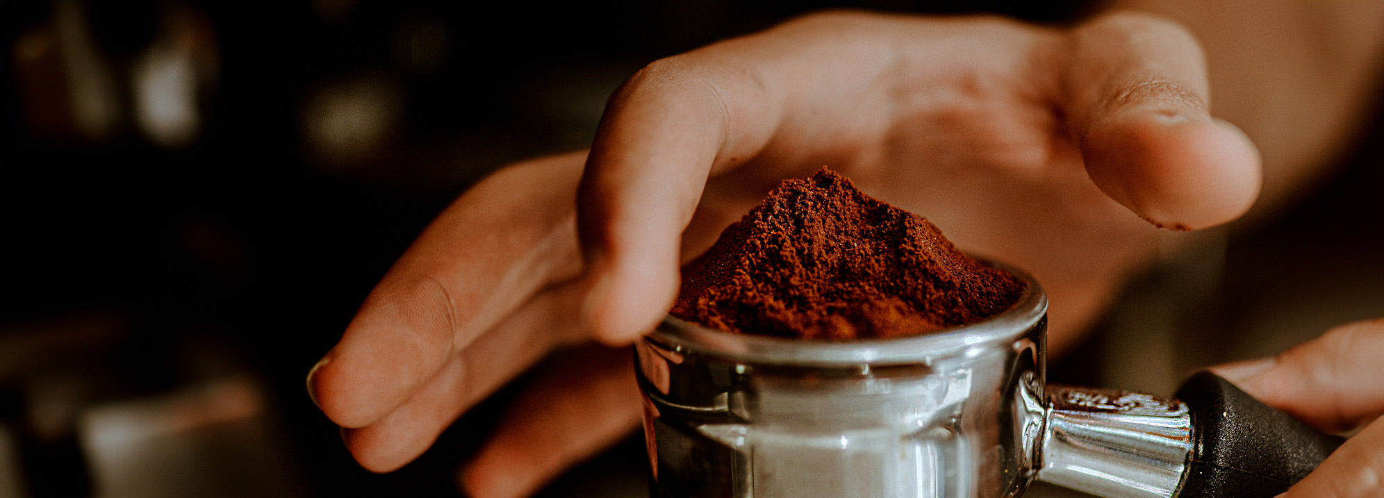 closeup of person holding portafilter and leveling coffee with finger.